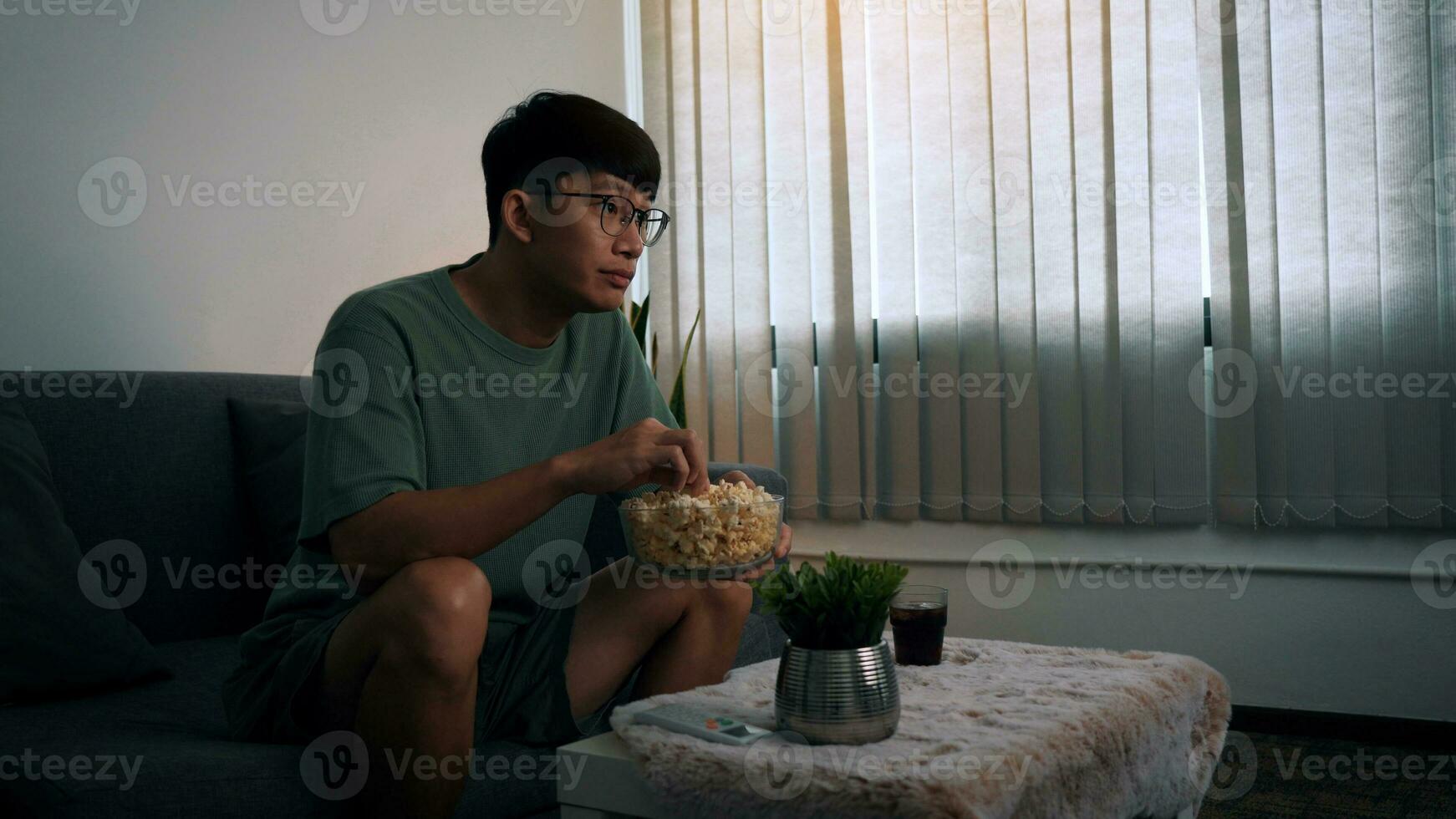 homme asiatique regardant une série de salon tout en mangeant un pop-corn la nuit. photo