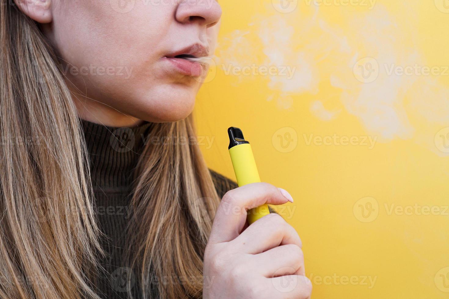 une jeune fille fume une cigarette électronique jetable photo