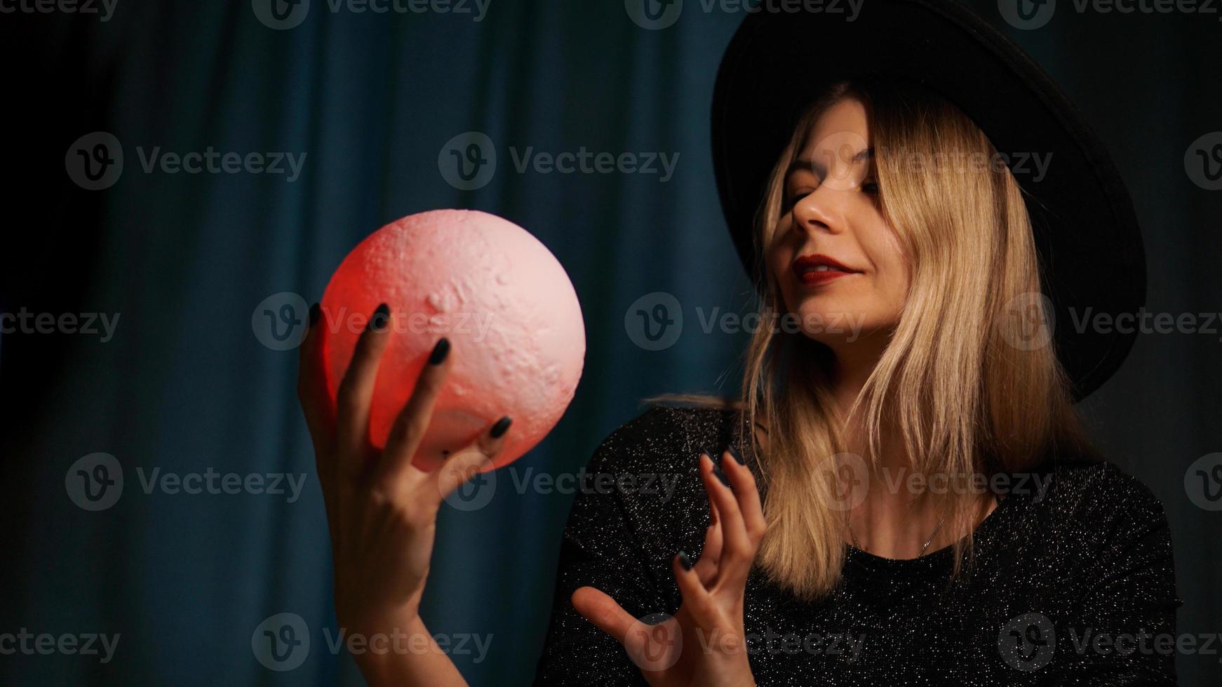 une jeune femme diseuse de bonne aventure dans un chapeau tient une boule magique. photo