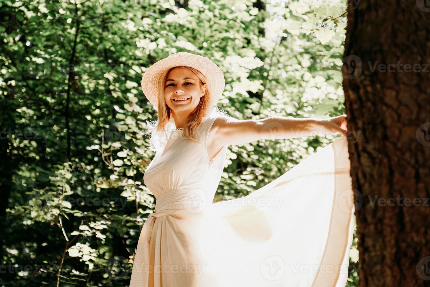 Jeune femme au chapeau de paille tenant l'ourlet de sa robe blanche photo