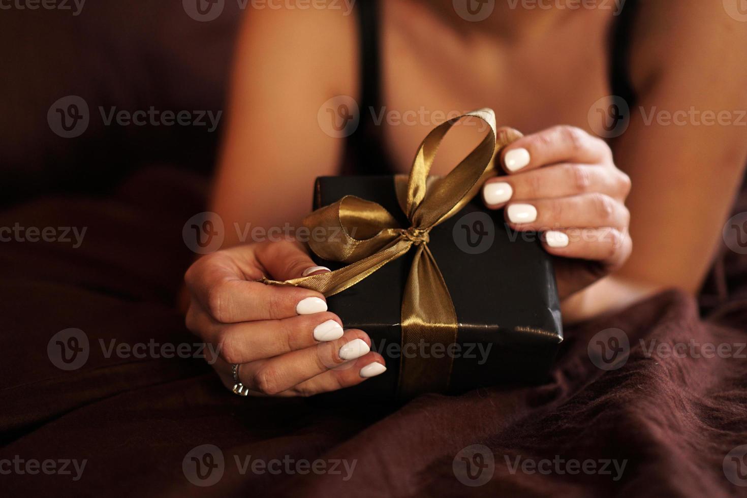 la femme ouvre un cadeau dans une boîte noire avec un ruban d'or photo