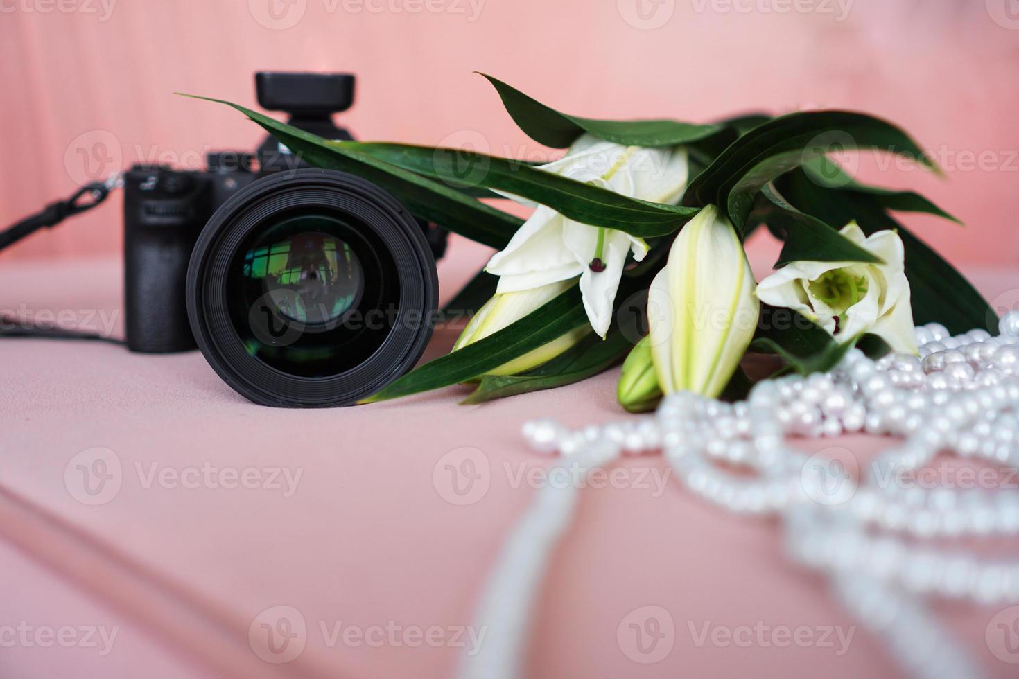 appareil photo noir avec un objectif et des lys blancs et un collier de perles