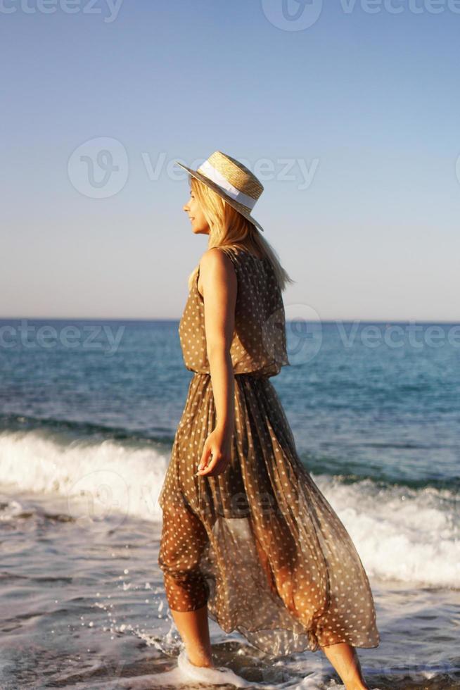 femme sur la plage dans une robe marron et avec un chapeau de paille photo