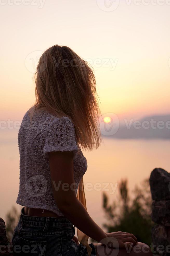 la fille regarde le coucher de soleil sur la mer depuis un point élevé. photo verticale