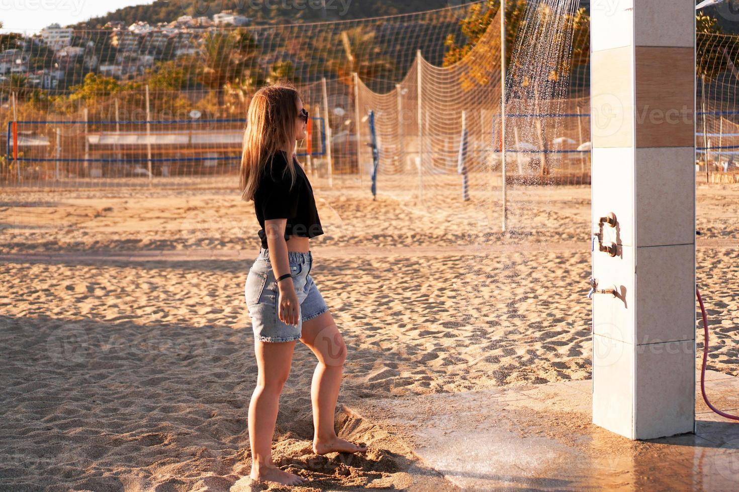 une fille en short et un t-shirt noir sur la plage près de la douche. photo