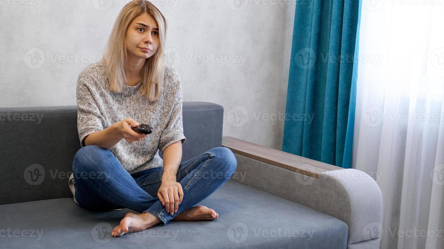 Jeune femme changeant les chaînes de télévision avec télécommande assise sur un canapé photo