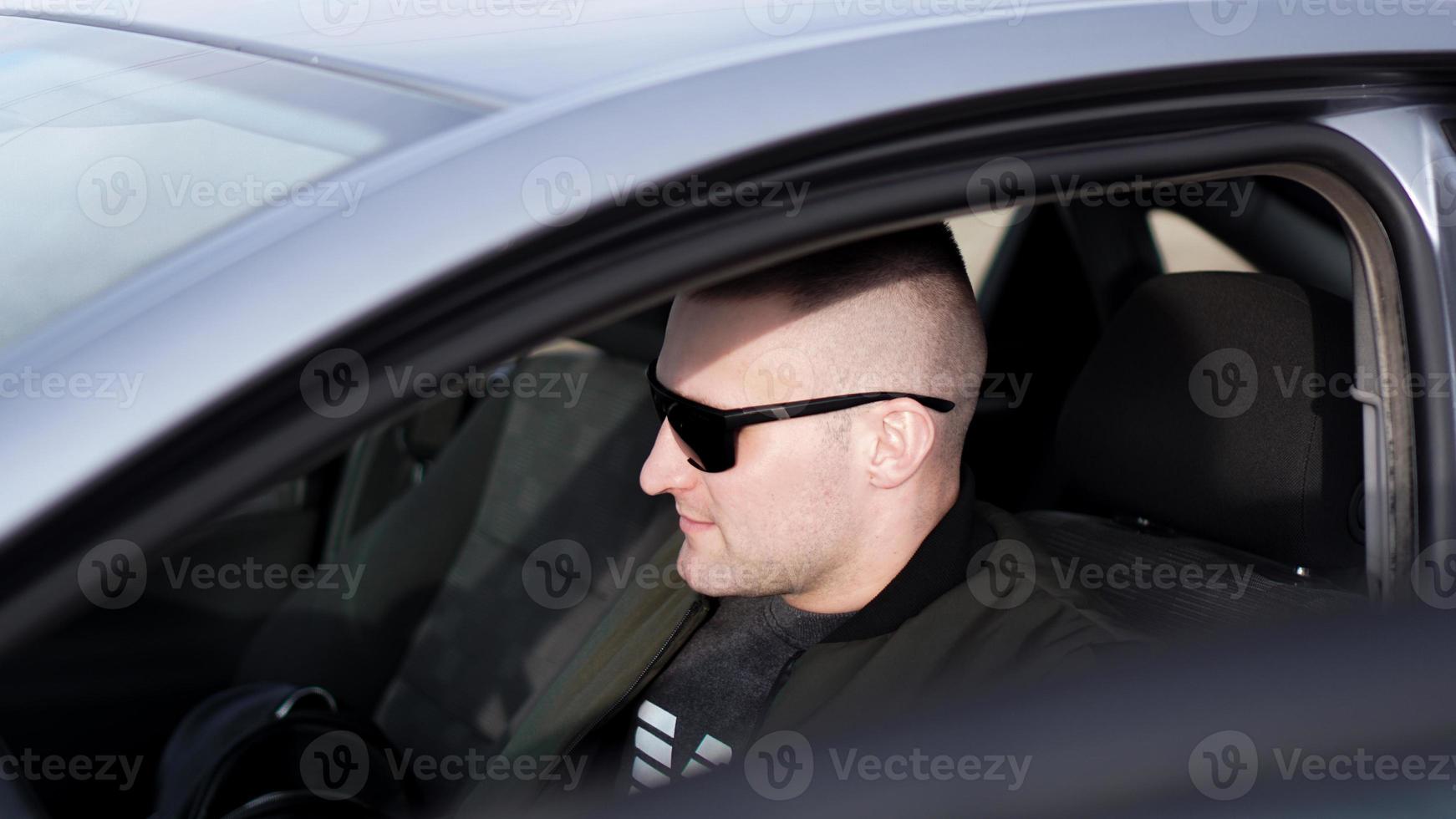 Vue latérale d'un jeune homme élégant et confiant à lunettes de soleil dans sa voiture photo