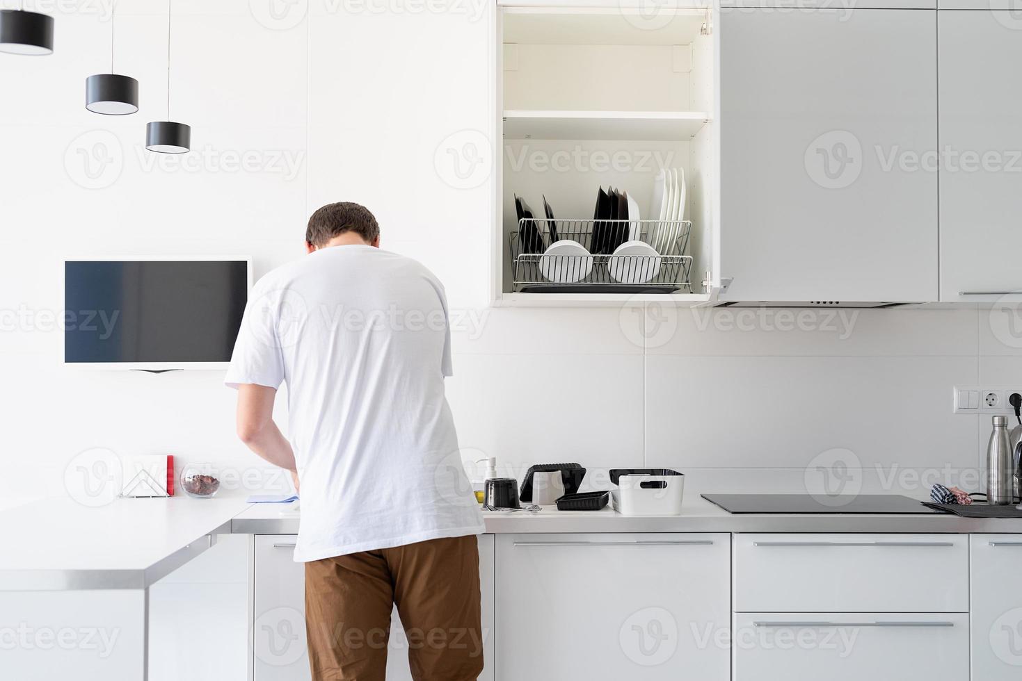 homme en t-shirt blanc laver la vaisselle dans la cuisine photo