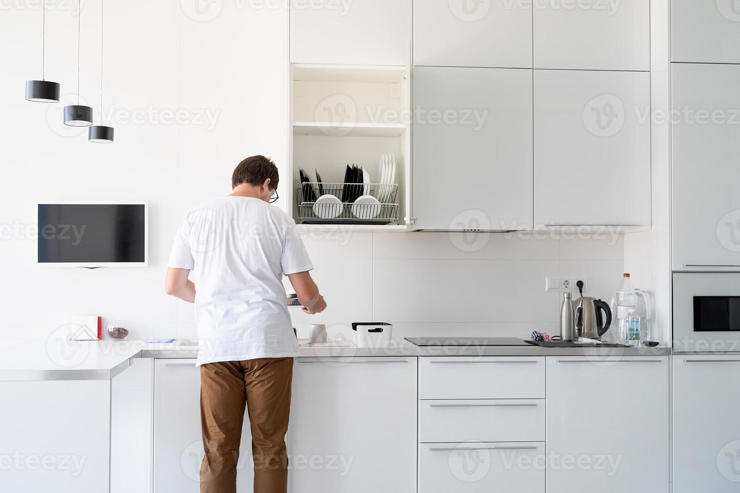 homme en t-shirt blanc laver la vaisselle dans la cuisine photo