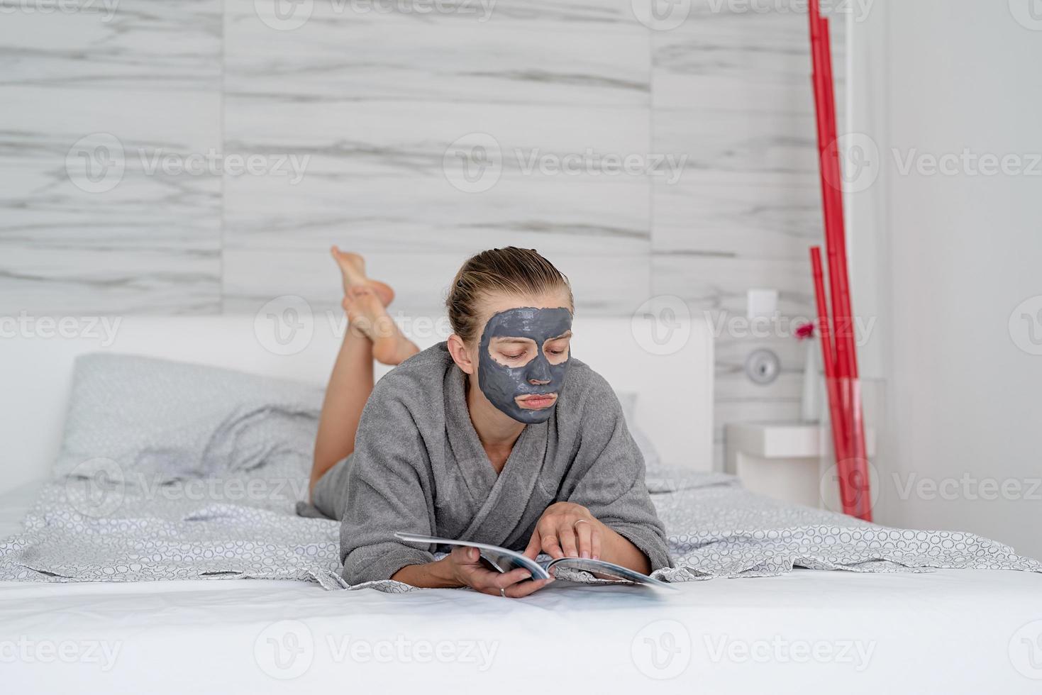 femme avec masque facial relaxant allongé sur le lit en lisant un magazine photo