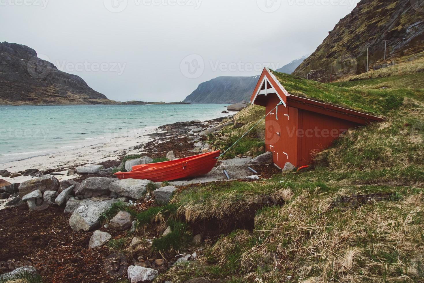 maison rouge avec de la mousse sur le toit et le bateau sur fond de mer et de montagne photo