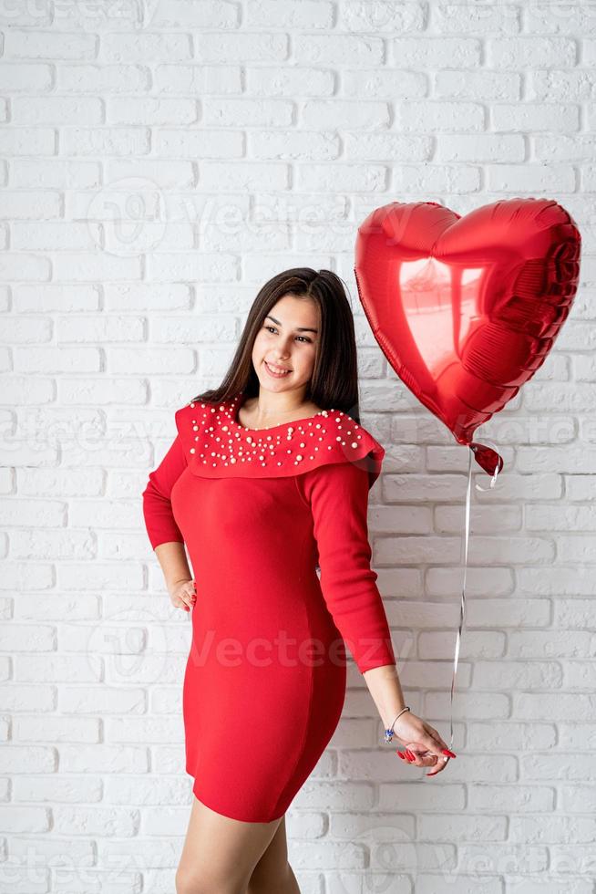 Jeune femme brune en robe rouge tenant un ballon coeur rouge photo
