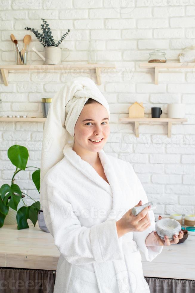 heureuse jeune femme appliquant un gommage sur son visage dans sa cuisine à domicile photo