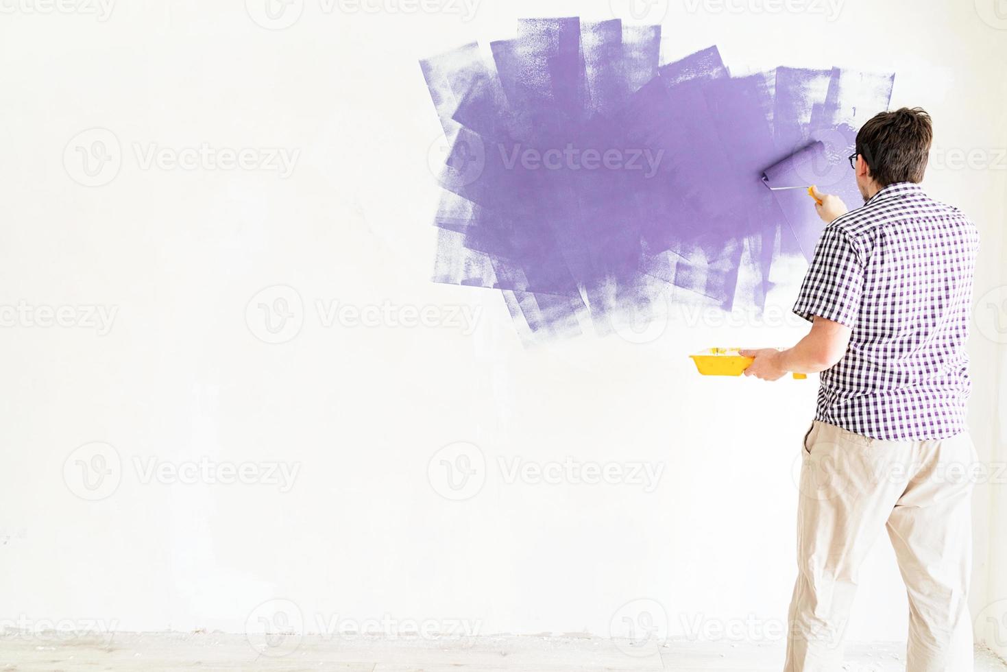 mur de coloration de l'homme avec un rouleau avec de la peinture violette photo