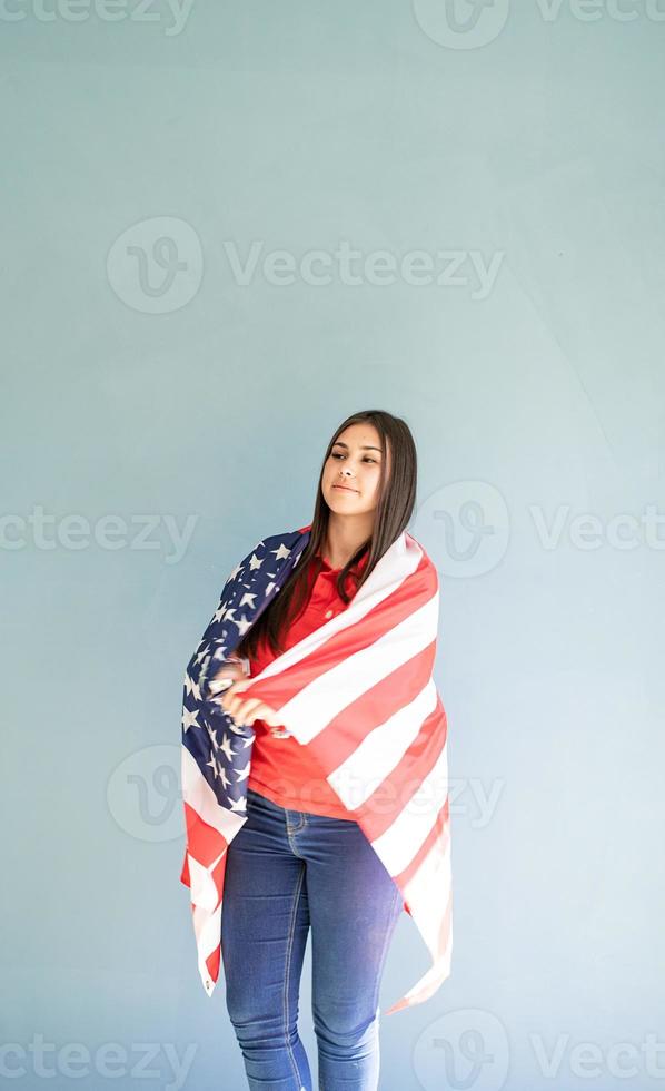 belle jeune femme enveloppée dans un drapeau américain sur fond bleu photo