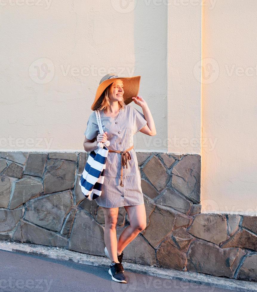 femme marchant dans la rue tenant son chapeau à la lumière du coucher du soleil photo