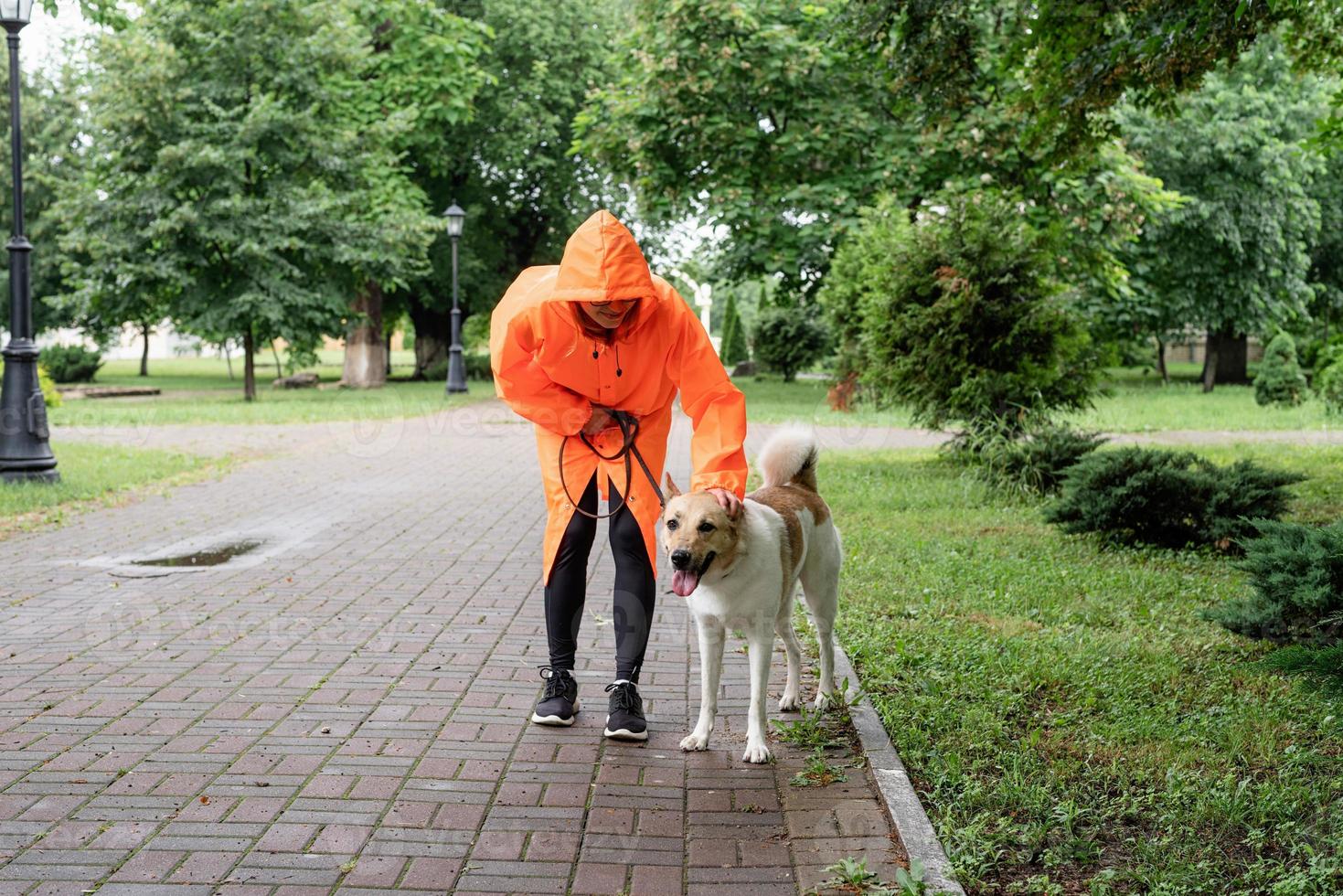 Jeune femme en imperméable orange marchant avec son chien dans un parc photo