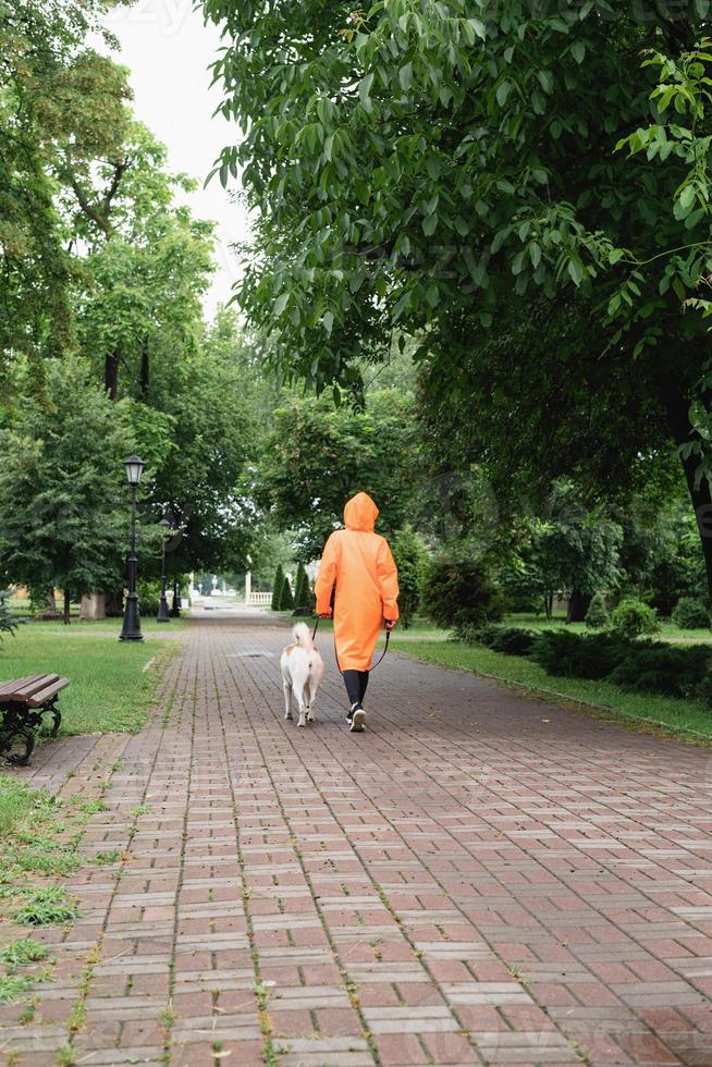 Jeune femme en imperméable orange marchant avec son chien dans un parc photo