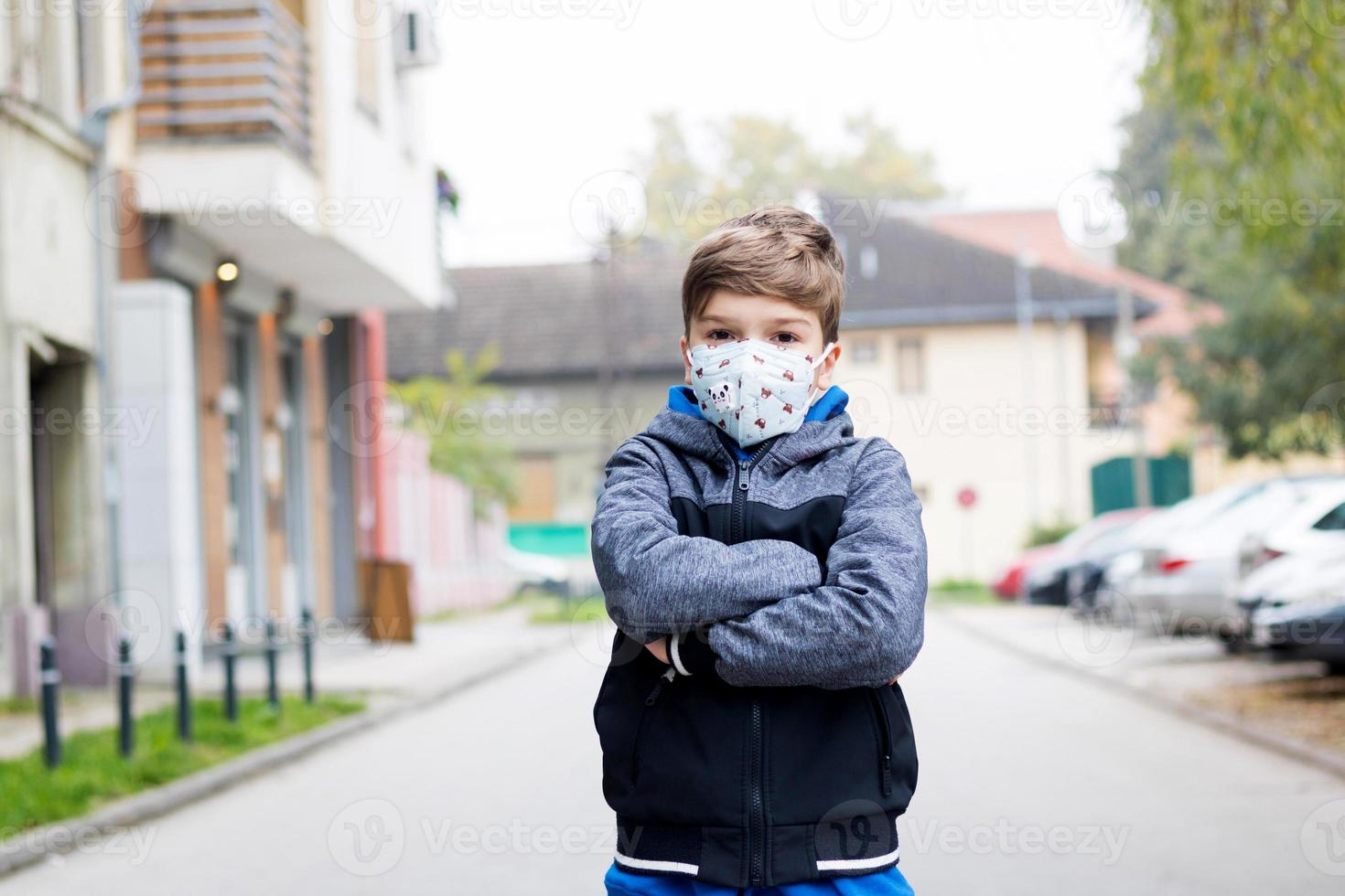 petit garçon aux bras croisés portant un masque facial kn95 à l'extérieur. photo