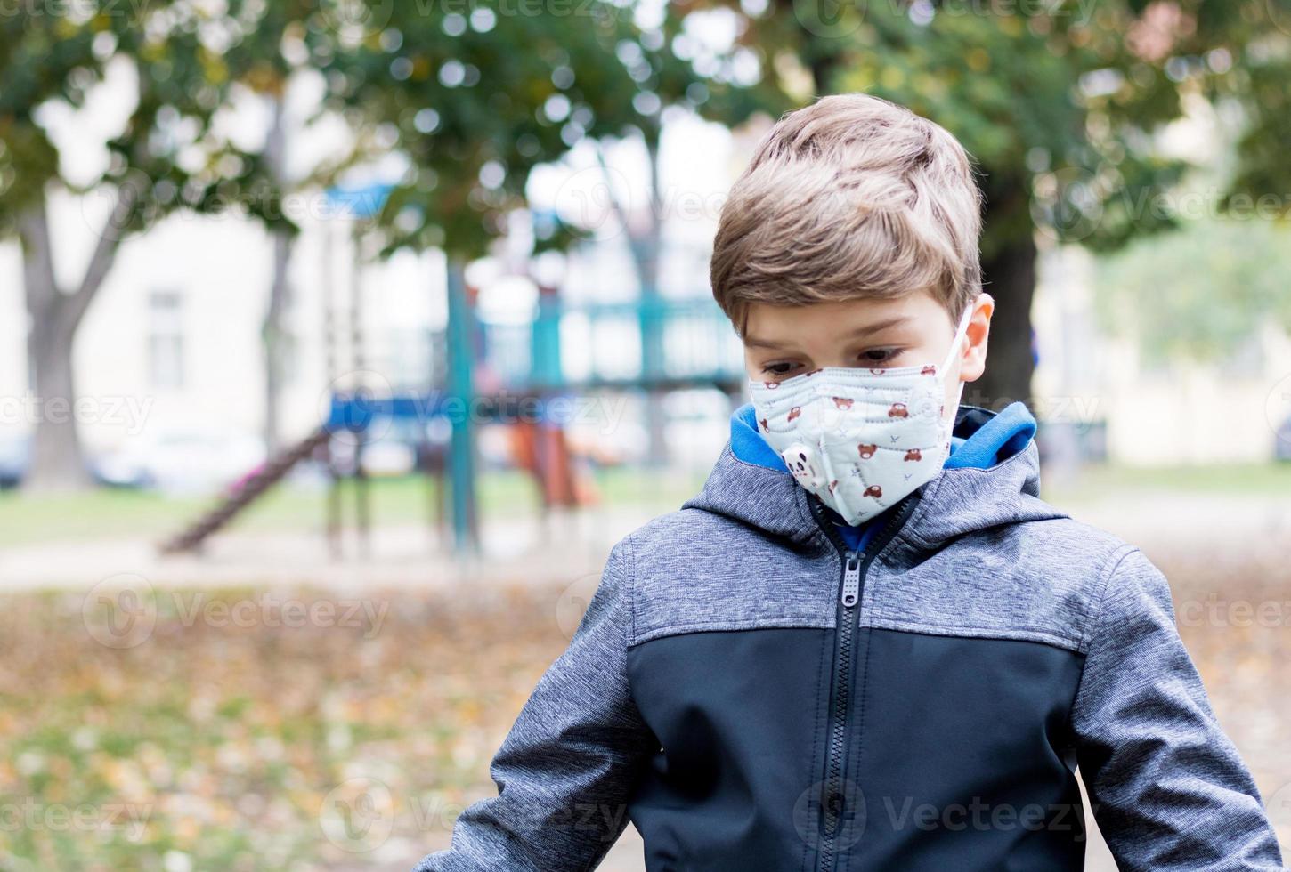 un garçon solitaire avec un masque facial se sent triste au terrain de jeu à cause du coronavirus photo