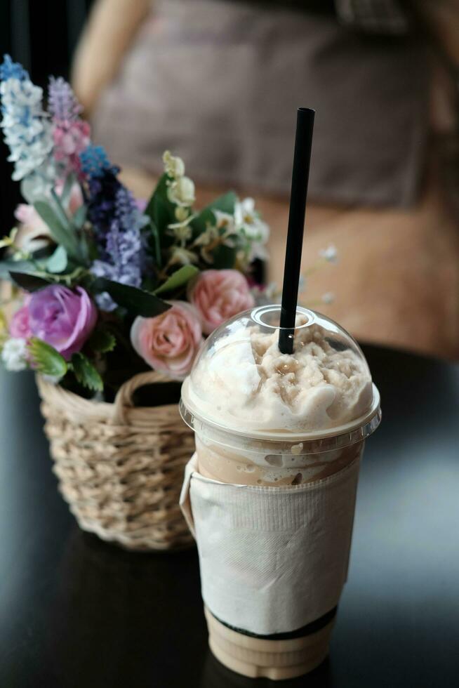 latté caramel Milk-shake café dans prendre une façon Plastique tasse et magnifique Plastique épanouissement Rose fleurs et flore bouquet dans tissé rotin panier décorer sur table dans café photo