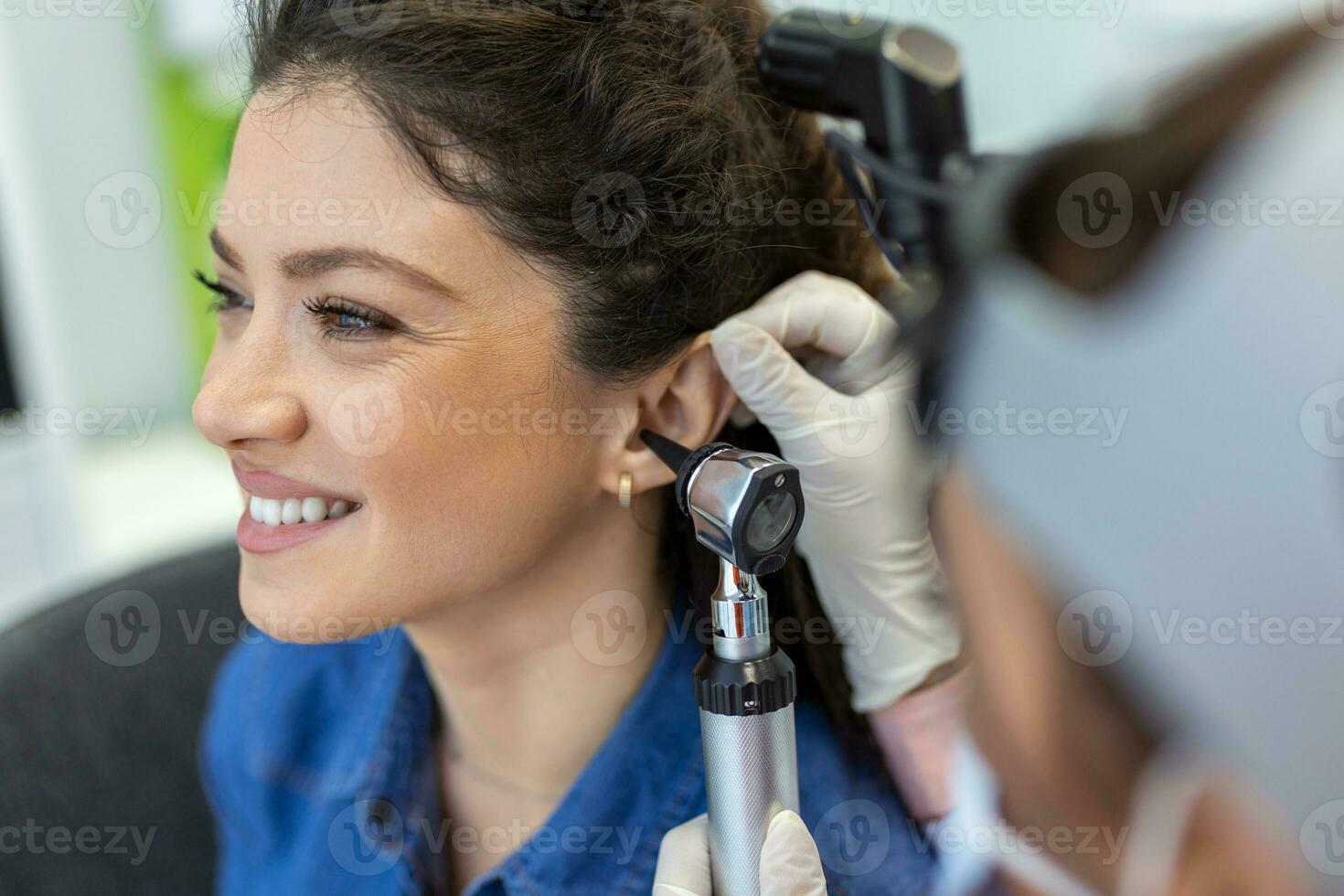 proche en haut de une femelle médecin soigneusement en portant le oreille de le sien patient à établir une plus clair vue de le à l'intérieur de le sien oreille, à voir si il a besoin audition sida à une moderne clinique photo