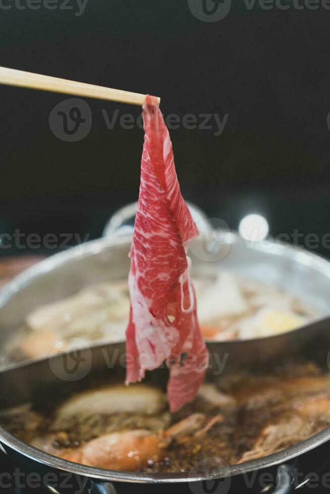 homme main prend brut délicieux du boeuf tranché mettre cuisine dans chaud bouilli soupe. photo