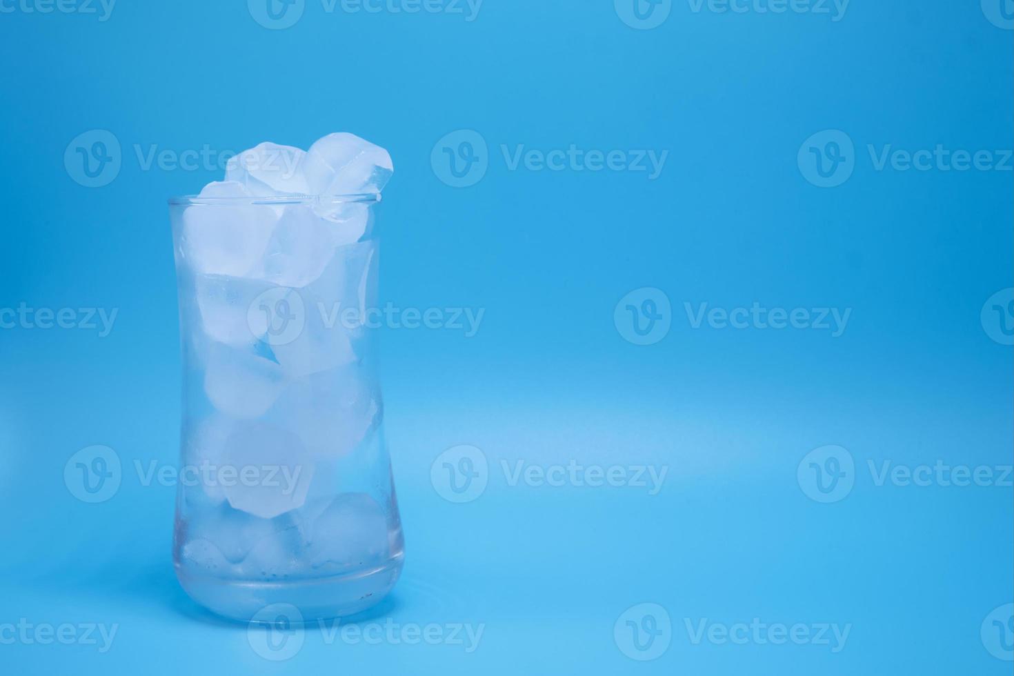 la glace dans un verre d'eau transparent fondant sur fond bleu. photo