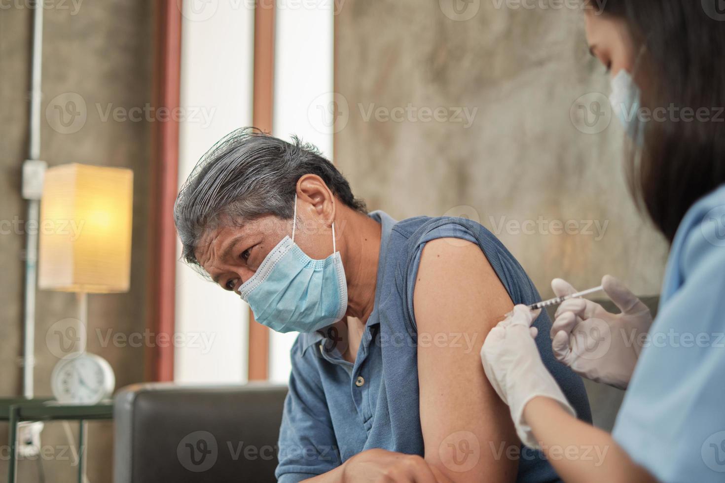 une femme médecin asiatique vaccine un homme âgé à la maison. photo