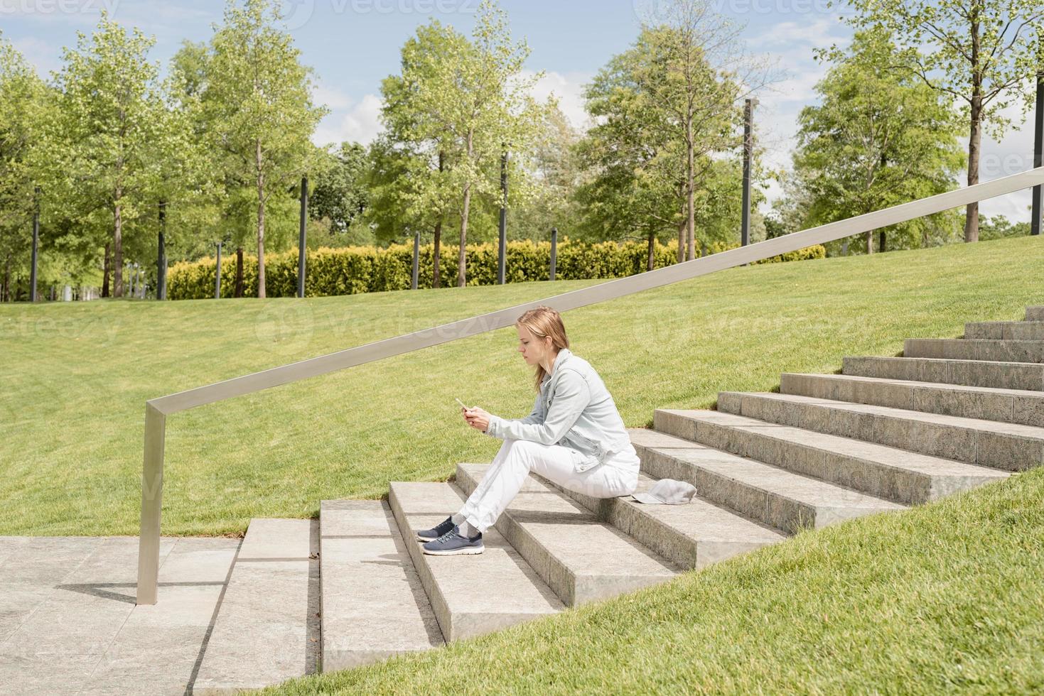 femme textos sur son téléphone portable, assise sur les escaliers dans le parc photo