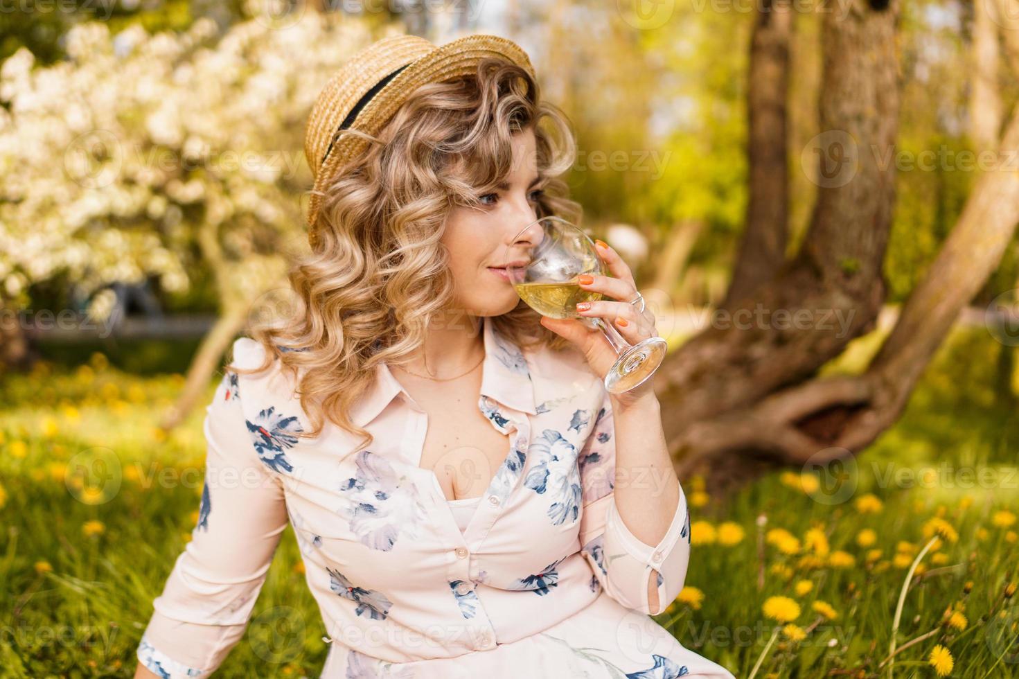 Belle jeune femme aux cheveux blonds au chapeau de paille boit du vin photo