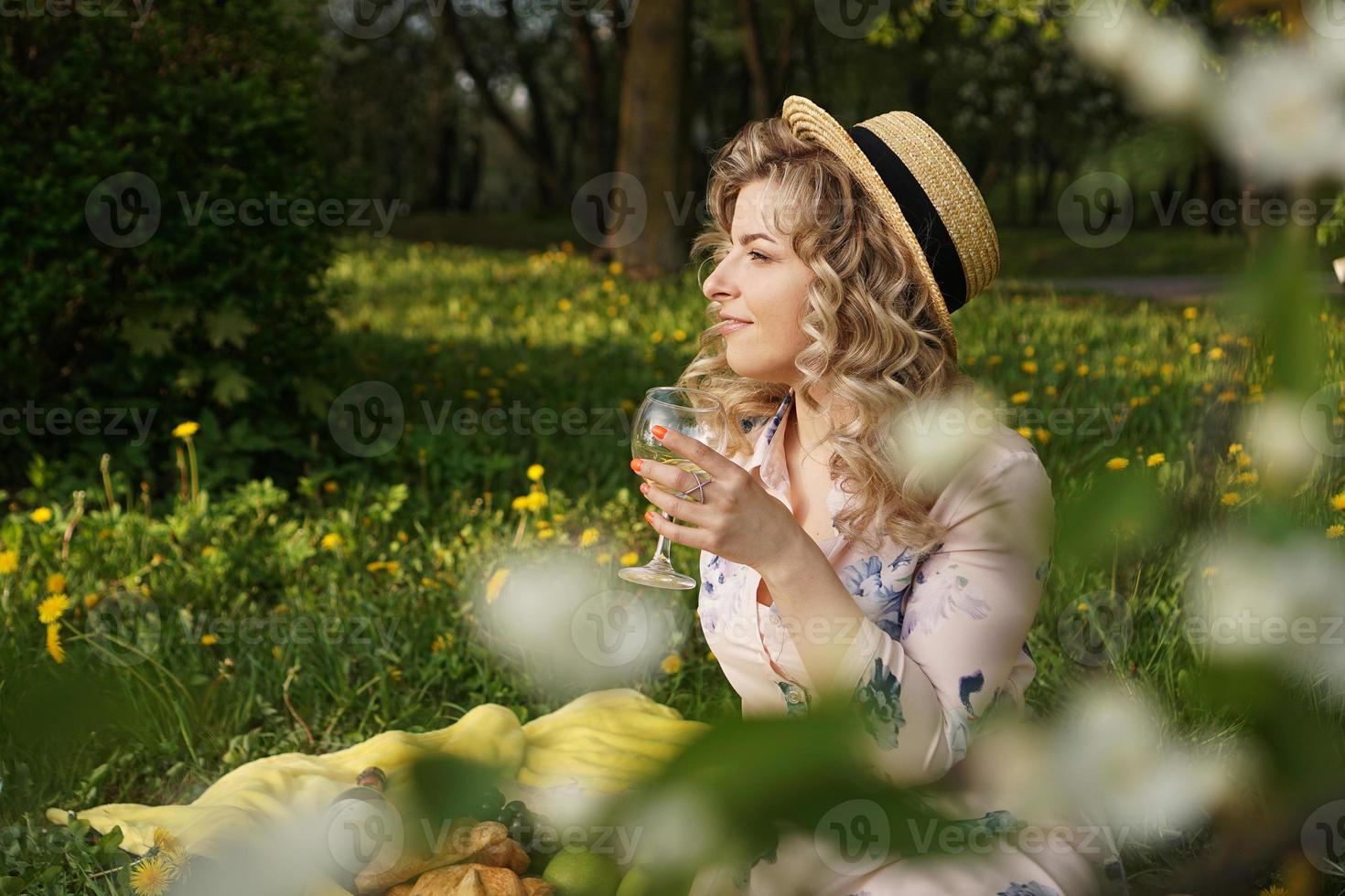 Belle jeune femme aux cheveux blonds au chapeau de paille boit du vin photo