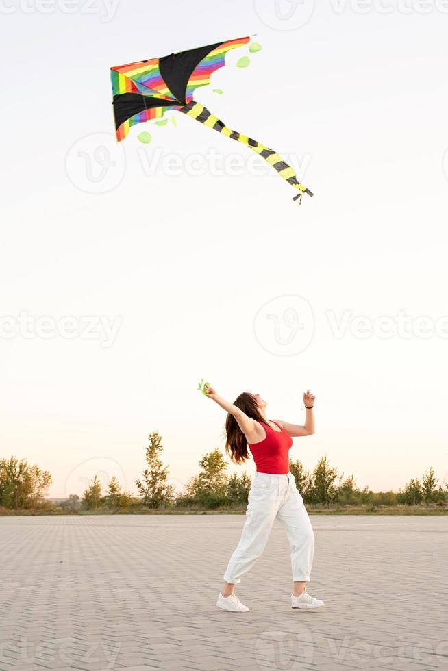 Jeune femme faisant voler un cerf-volant dans un parc public au coucher du soleil photo