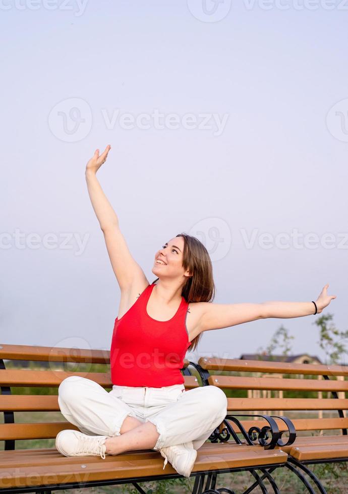 heureuse jeune femme assise sur un banc avec les jambes croisées photo