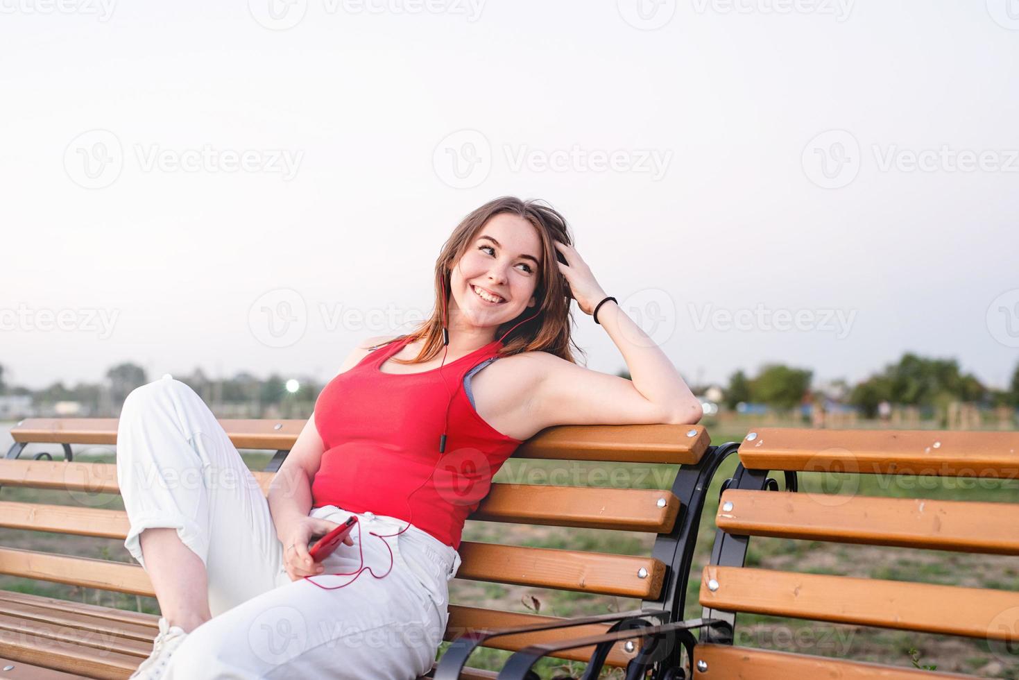 heureuse jeune adolescente assise sur un banc dans le parc à l'écoute photo