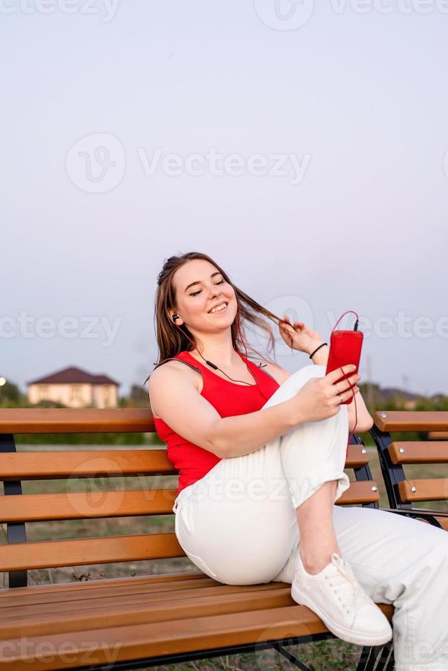 heureuse jeune adolescente assise sur un banc dans le parc à l'écoute photo