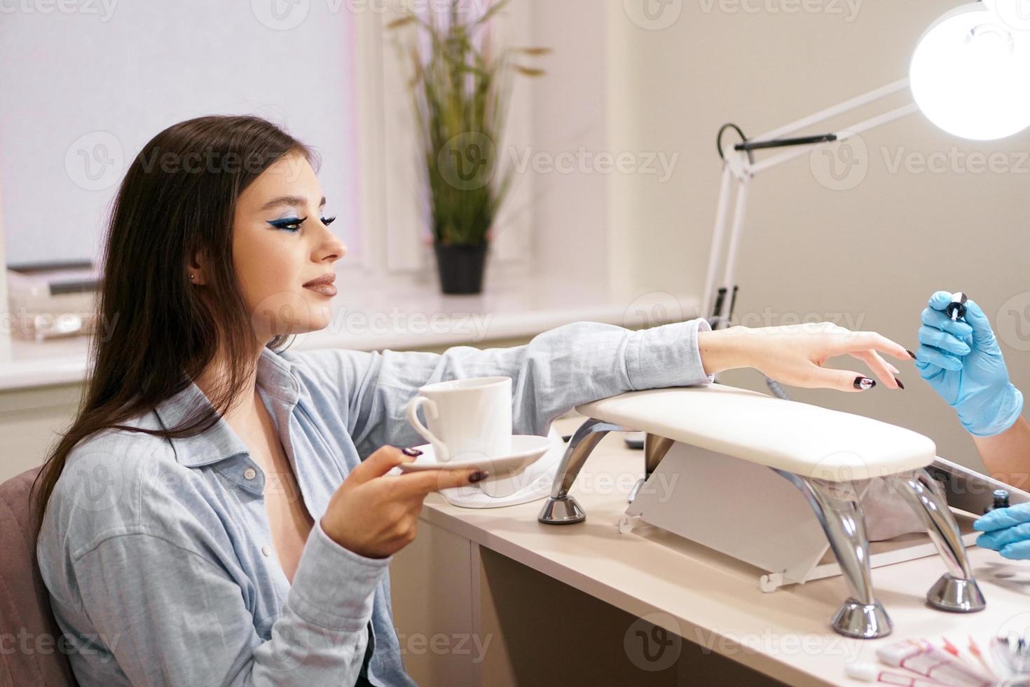 femme se faire manucure dans le salon et détient une tasse de café blanche photo