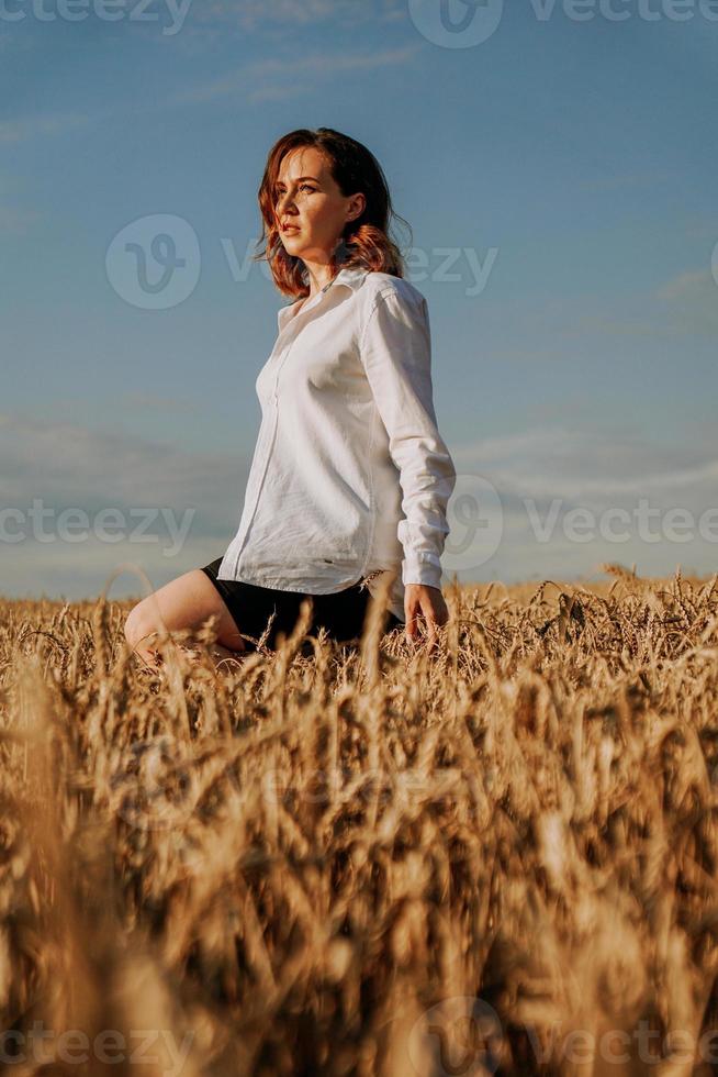 heureuse jeune femme en chemise blanche dans un champ de blé. journée ensoleillée. photo