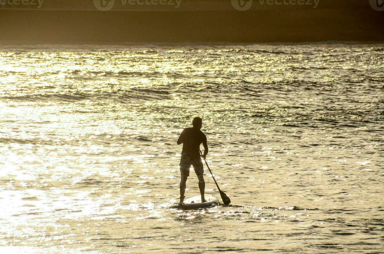 une homme est permanent sur une pagayer planche dans le l'eau photo