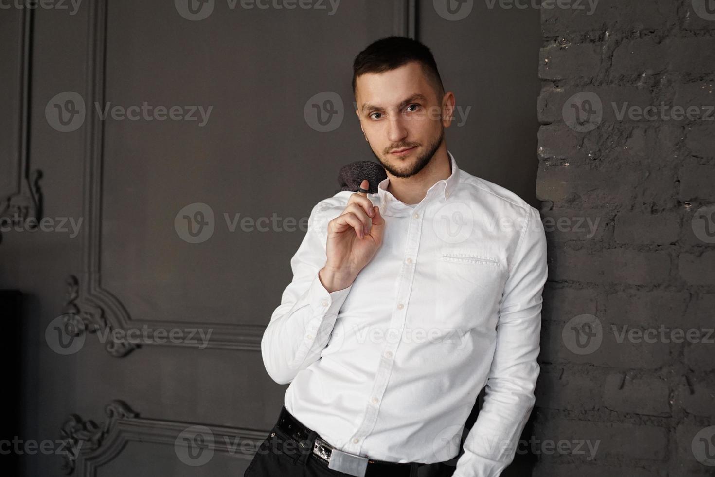 jeune homme d'affaires élégant en chemise blanche tient une veste sur le doigt photo