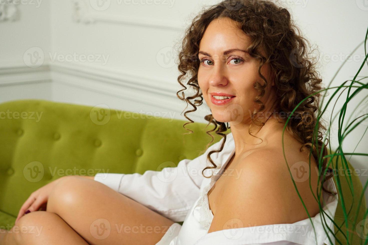 heureuse jeune femme aux cheveux bouclés en chemise blanche à la maison photo