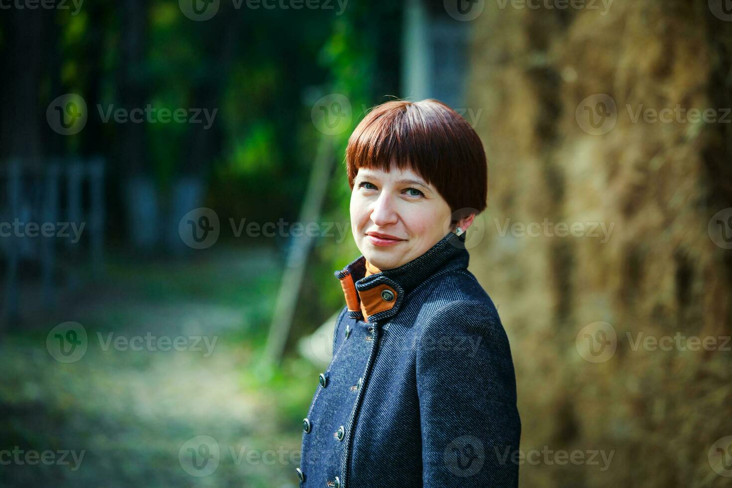 une Jeune femme avec court marron cheveux des promenades par le campagne. une femme est permanent près une meule de foin. photo