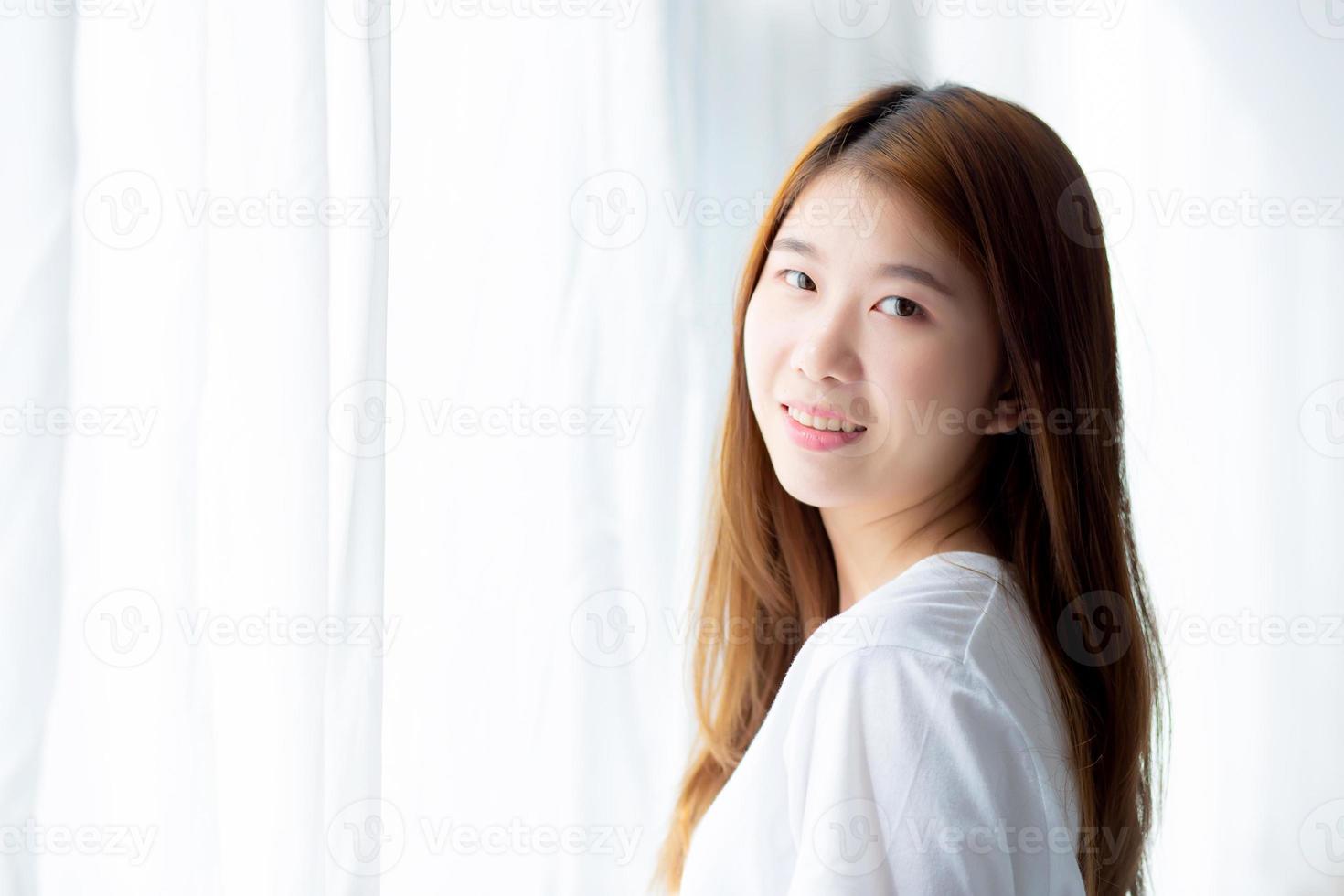 portrait d'une belle jeune femme asiatique debout devant la fenêtre et souriante en se réveillant avec le lever du soleil le matin, concept de mode de vie et de détente. photo
