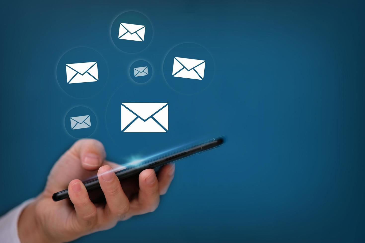 main utilisant un smartphone avec envoi d'e-mails sur fond bleu photo