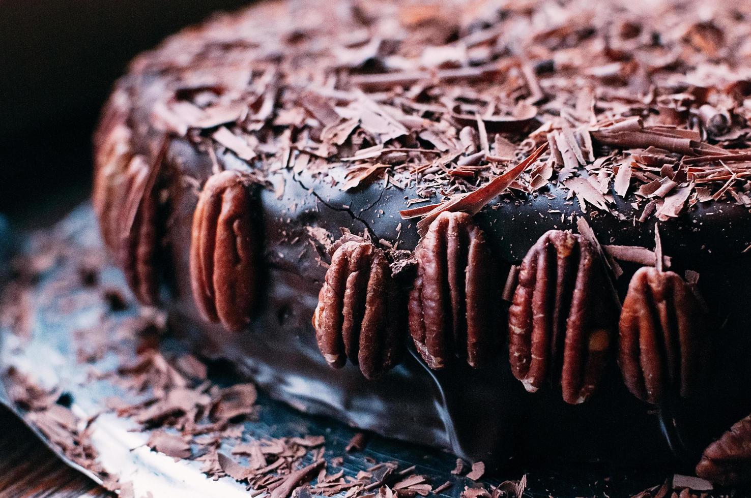 vue macro d'un gâteau au chocolat noir entier avec un beau glaçage, des chips et des noix de pécan sur le côté du plat en métal. mise au point sélective. glaçure luxueuse. image pour menu ou catalogue de confiserie photo