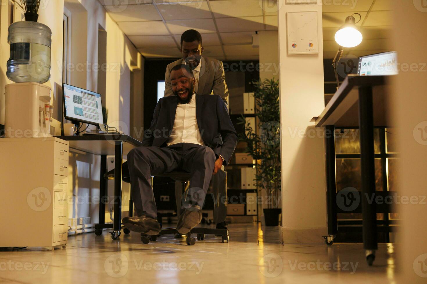 de bonne humeur africain américain gestionnaires ayant des sports course compétition dans moderne Commencez bureau, prise Pause de travail et ayant amusement. de bonne humeur des employés dans formel costume profiter équitation bureau chaise photo