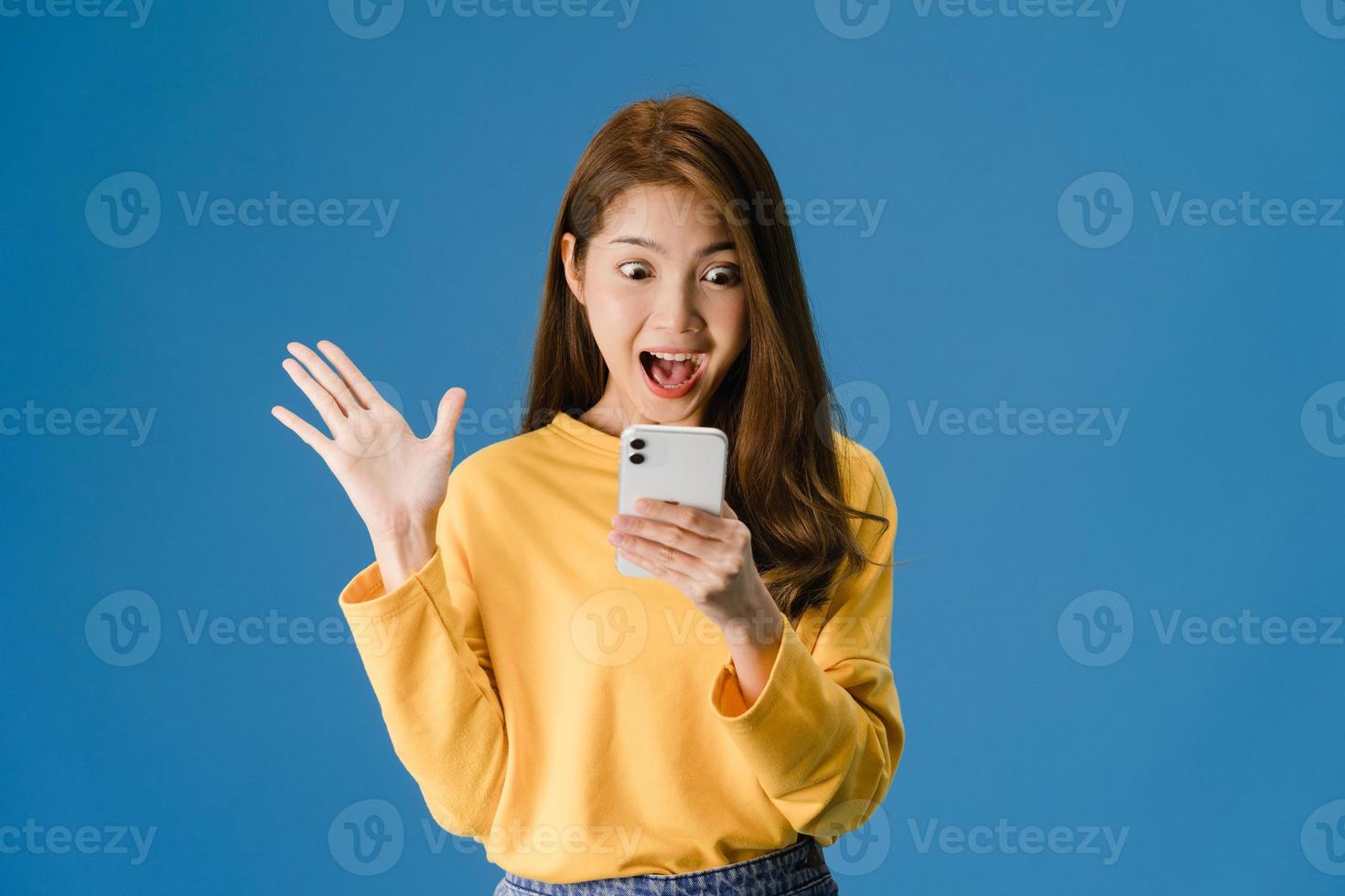 jeune femme utilisant un téléphone avec une expression positive sur fond bleu. photo