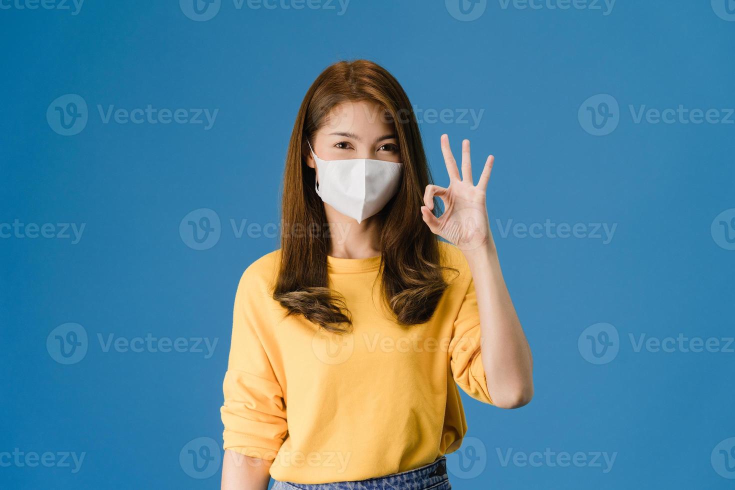 jeune fille asiatique porte un masque facial gesticulant signe ok sur fond bleu. photo