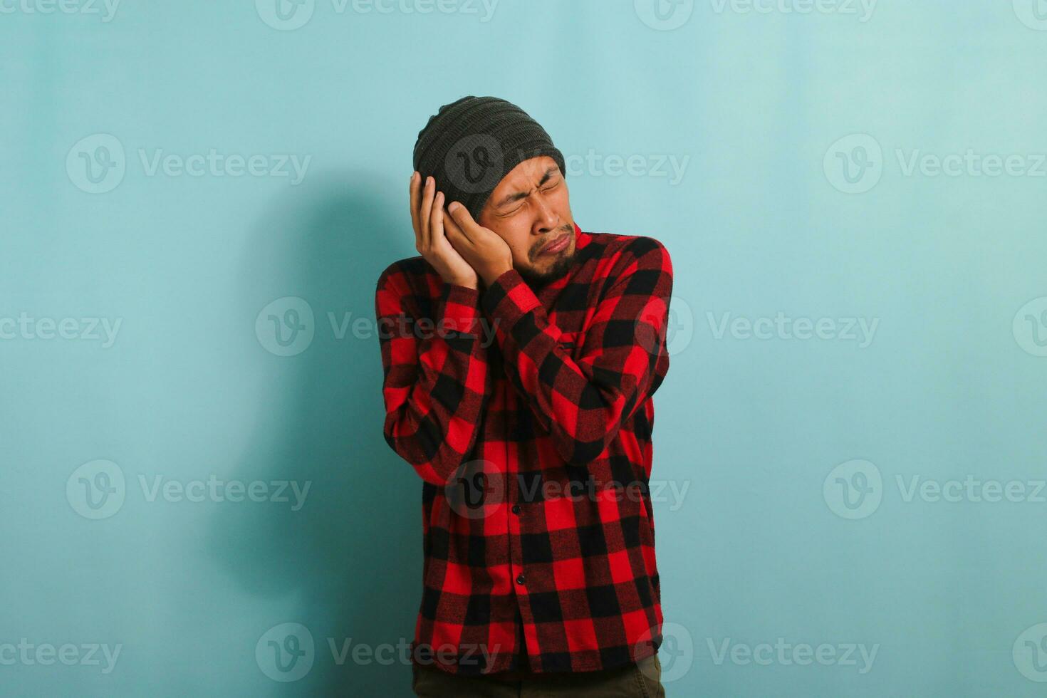Jeune asiatique homme détient le sien main près le sien oreille, Souffrance de mal d'oreille, isolé sur bleu Contexte photo