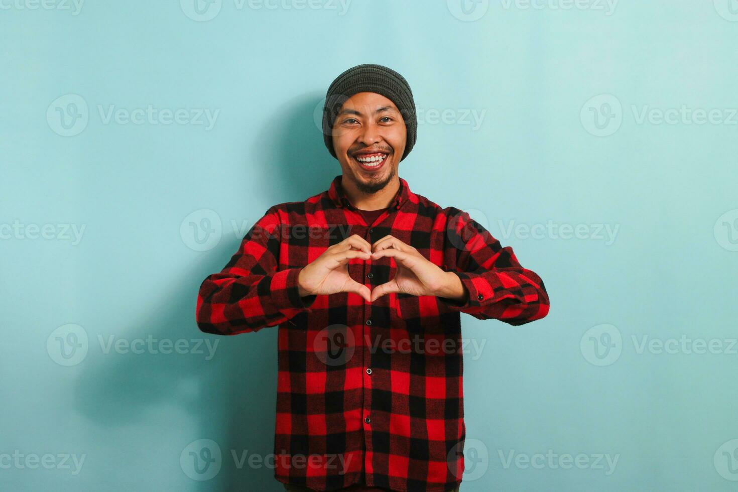 souriant Jeune asiatique homme spectacles une l'amour geste avec le sien main tandis que permanent contre une bleu Contexte photo